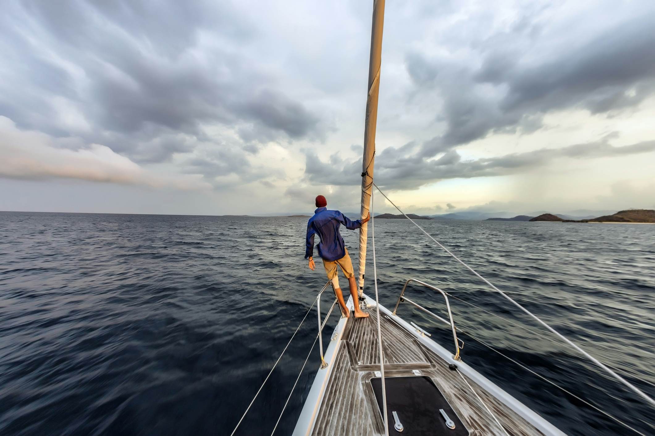 Rear view shot of single white man standing on bow of yacht looking out across Lombok, Indonesia